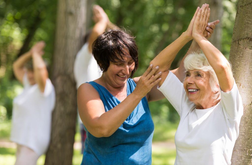 Instructor helping happy senior with yoga pose outside at senior community.