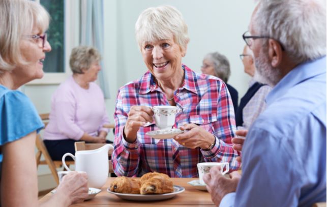 Happy seniors sitting at dinning table socializing with one another while having cup of tea