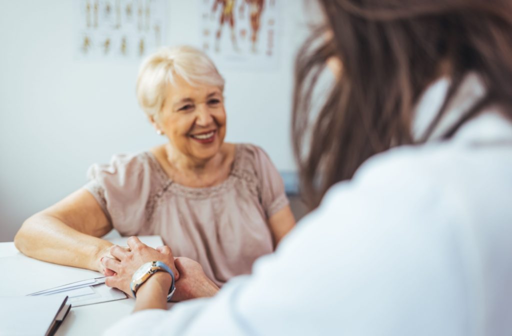 A doctor holds the hand of a smiling older woman during an appointment.