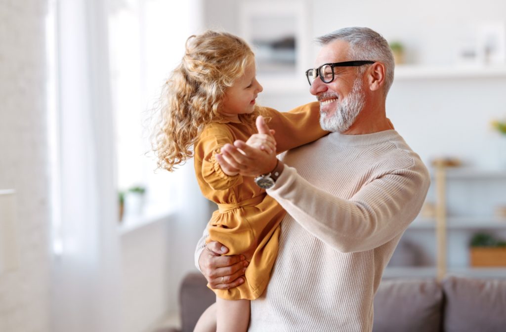 A smiling senior holds their grandchild in their arms, dancing with them at their senior living community