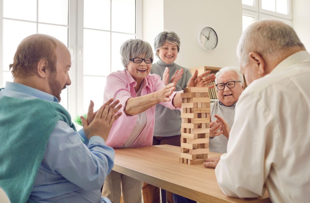 Seniors gathered at a table playing Jenga smiling and clapping in a bright inviting room promoting active and social living