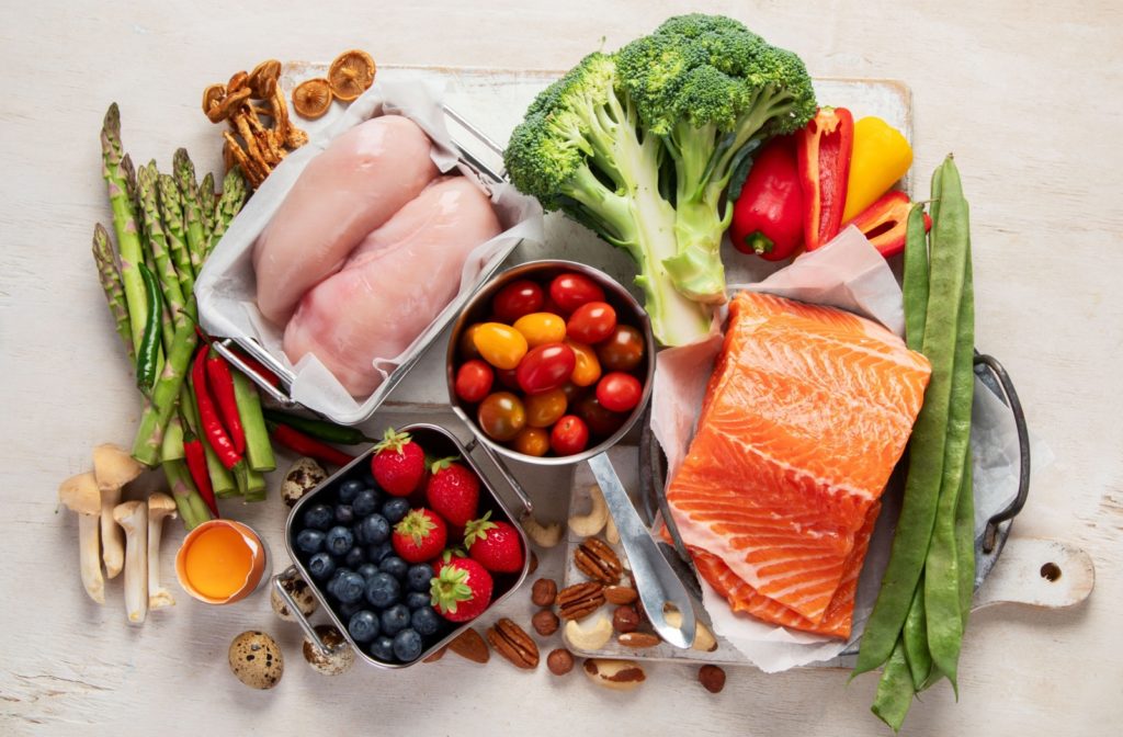 A selection of keto-friendly foods for seniors, including fresh vegetables, salmon, chicken, and berries, arranged on a wooden surface to emphasize a balanced and nutritious diet