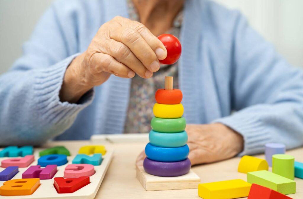 A senior with dementia works on several colorful puzzles as part of exercises to strengthen cognitive skills in memory care