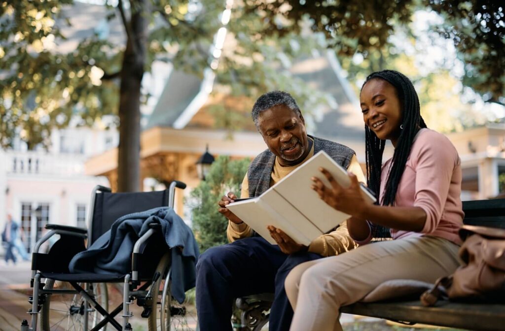An adult shows their older parent a photo album on a visit to their senior living community as they enjoy a moment outside